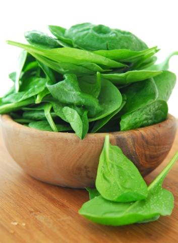 Fresh spinach iin a wooden bowl on a cutting board